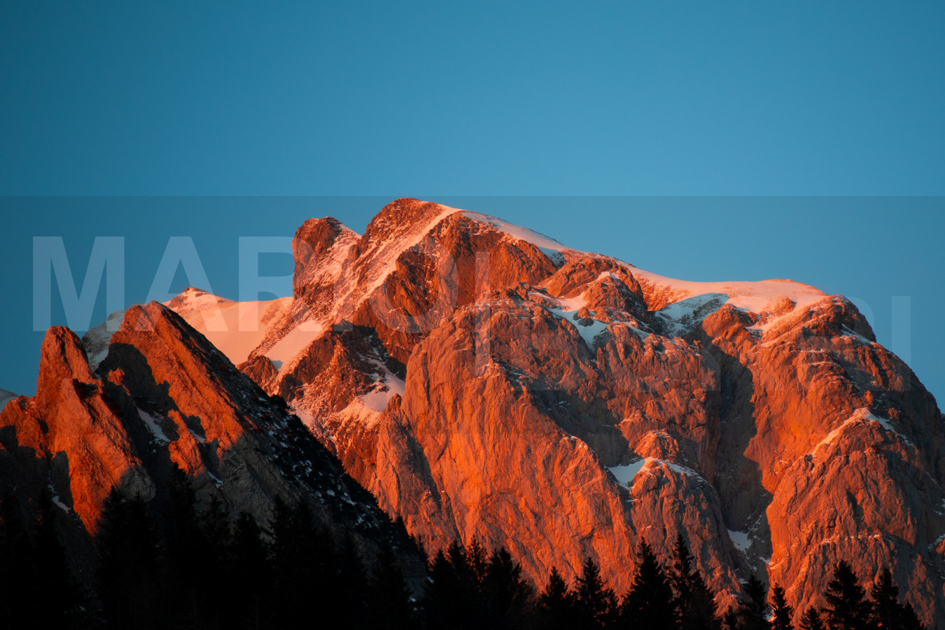 Alpine Landschaft in Wildhaus SG bei Sonnenaufgang oder Sonnenuntergang mit rot leuchtenden, schneebedeckten Gipfeln.