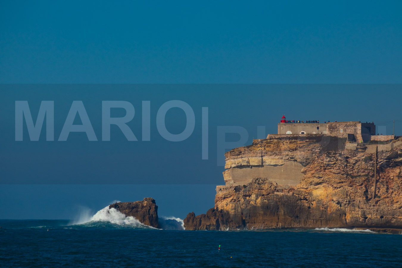 Leuchtturm von Nazaré auf einer Felsklippe mit brechenden Wellen im Atlantik.