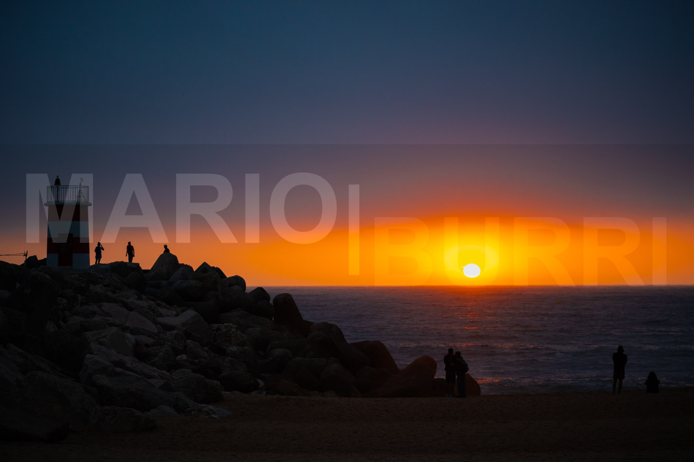 Ein ruhiger Sonnenuntergang über dem Meer, mit einer leuchtenden goldenen Sonne am Horizont und einem Himmel in warmen Orange-, Gelb- und Blautönen. Foto von MARIO|BURRI.